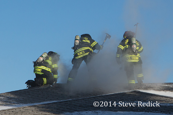 firemen work to ventilate roof of house on fire