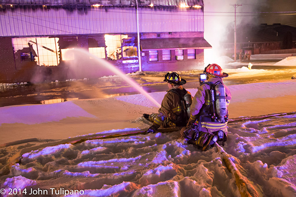 firemen with hose at huge night time fire