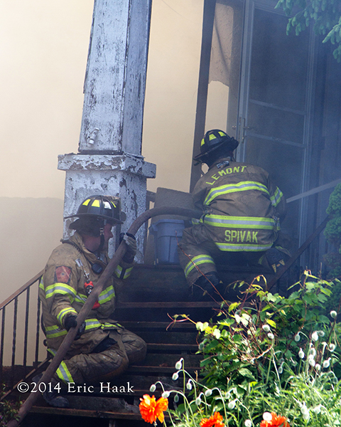 firemen with hose on steps of house
