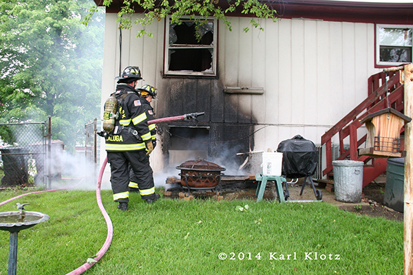 fireman with hose and charred siding on house