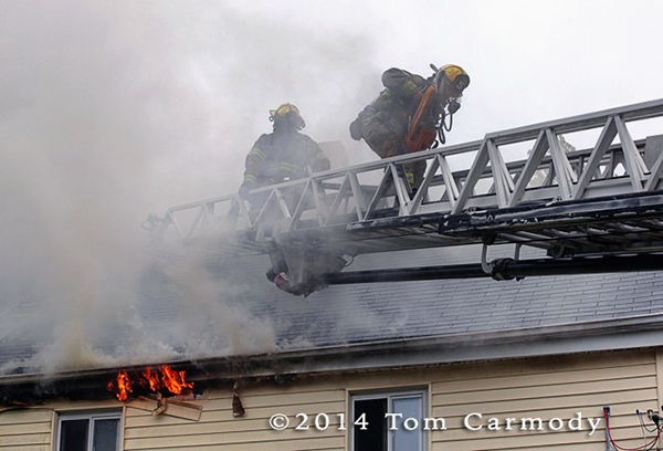 firemen on aerial ladder leaving roof in heavy smoke
