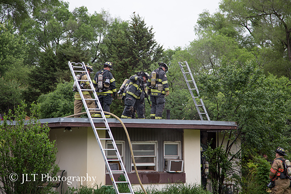 firemen work on the roof of a house after a fire