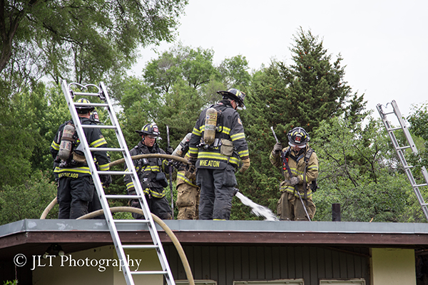 firemen work on the roof of a house after a fire