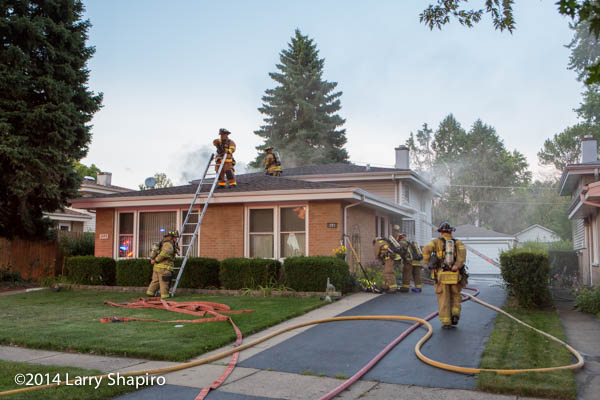 firemen climb to the roof of a house to ventilate the smoke during a fire
