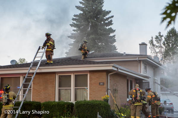 firemen climb to the roof of a house to ventilate the smoke during a fire