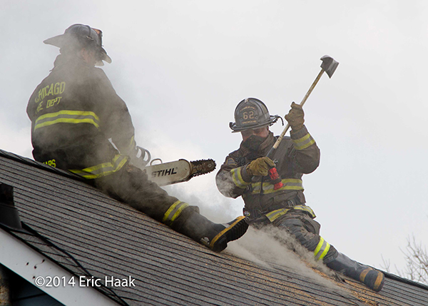 firemen with axes venting peaked house roof during fire