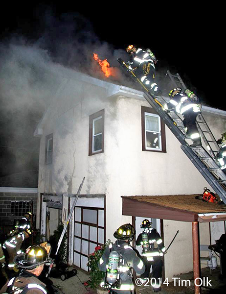 firemen climb ladder to roof of burning house