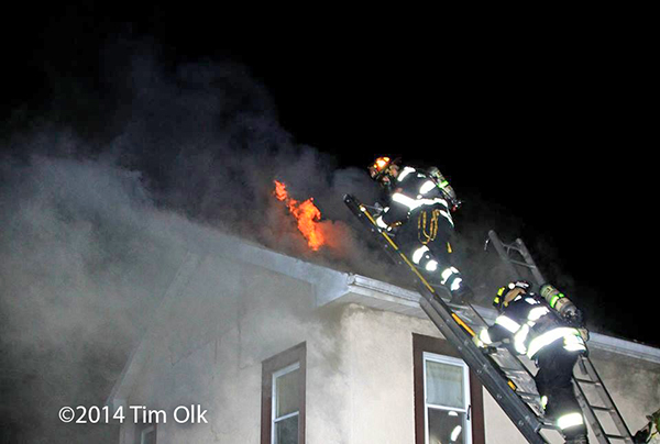 firemen climb ladder to roof of burning house