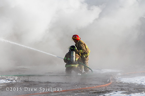 firemen with hose in smoke at fire scene
