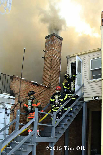 firemen with hose on building's back steps