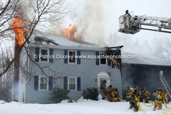 flames through the roof of a two-story house