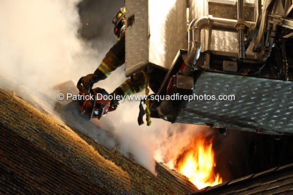 fireman vents roof at night with flames