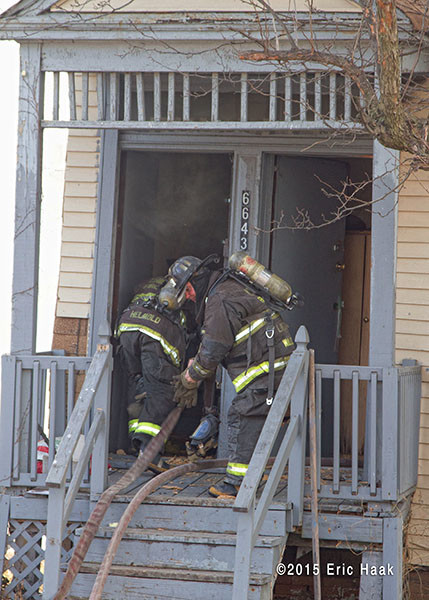 firemen take hose into burning house