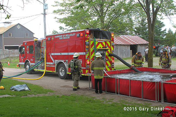 firemen dump water from a tender into a portable tank at a fire scene
