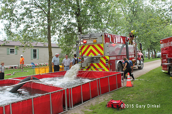 firemen dump water from a tender into a portable tank at a fire scene
