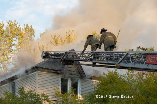 firemen climb aerial to vent house roof during fire