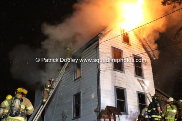 firemen on ladder at house fire at night with flames