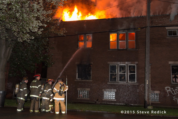 flames through the roof of a two-story building