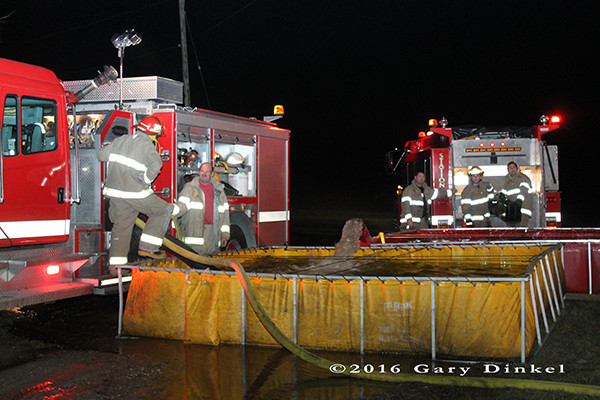 firefighters draft water from a portable tank at a rural fire scene