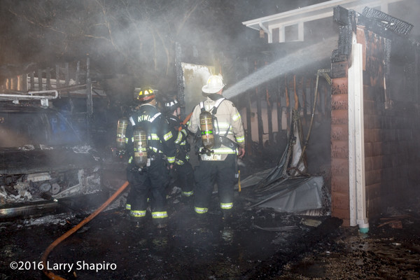 firefighters wash down the aftermath of a house fire in a rain storm