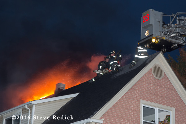 firemen on peak roof with fire at night