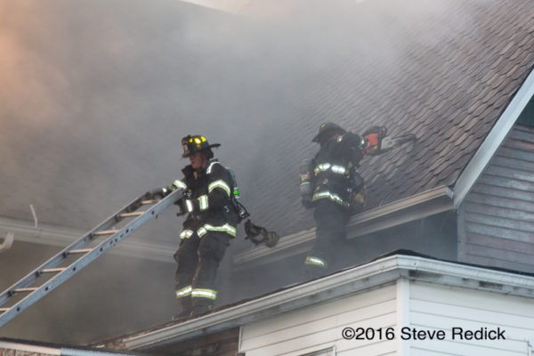 firefighters on house fire roof with smoke