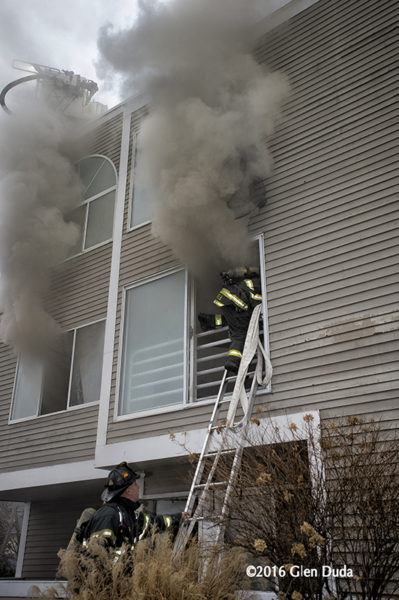 firefighter enters window from ladder with smoke