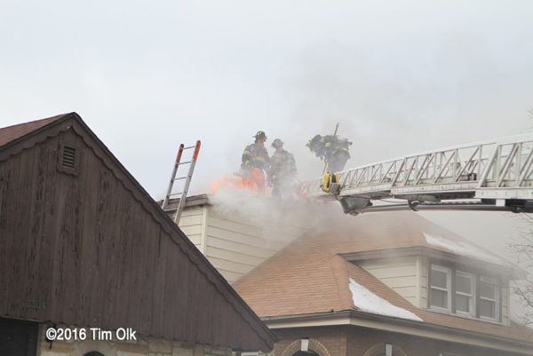 Firefighters venting roof with flames and smoke