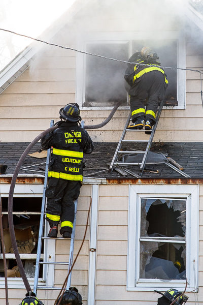 firefighters work from ground ladders at fire