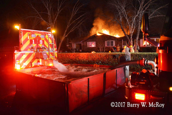 fire department water tender dumps into portable tank with house on fire