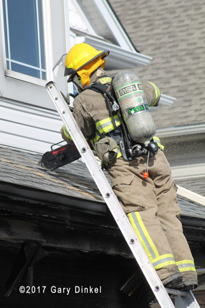 firefighter vents roof with saw from ladder