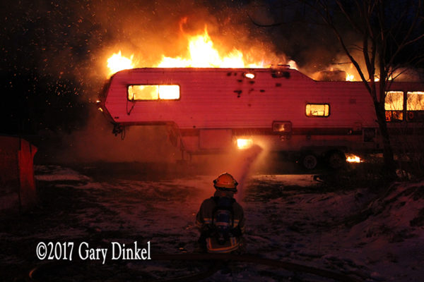 firefighter battles a recreational trailer engulfed in fire