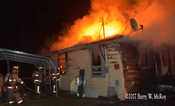heavy flames through roof of rural house at night