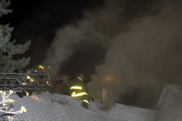 firefighters vent roof at night with heavy smoke