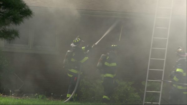 firefighters engulfed in smoke operate a hose line