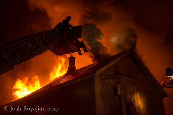 heavy flames and smoke through roof of a house at night