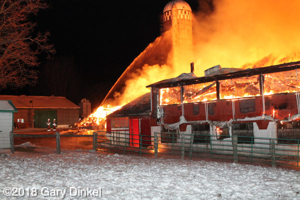 firefighters battle a barn fully engulfed in fire at night