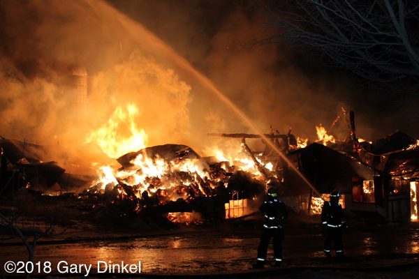 firefighters battle a barn fully engulfed in fire at night