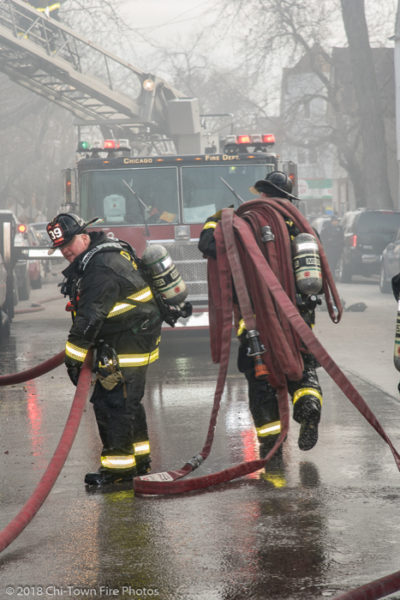 Firefighters carry hose in the street
