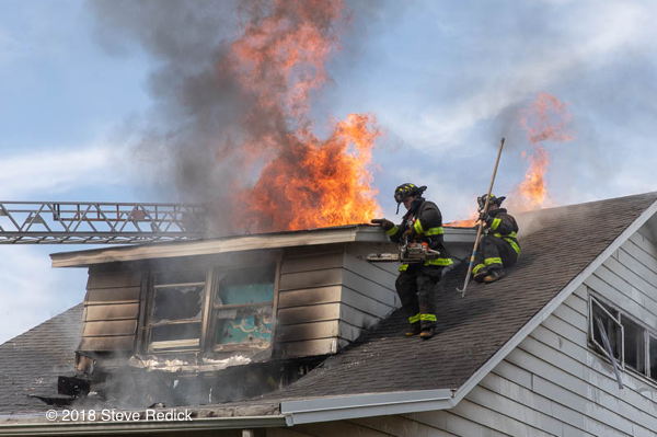 Firefighters vent house fire roof with flames