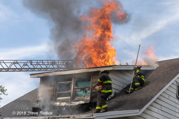 Firefighters vent house fire roof with flames