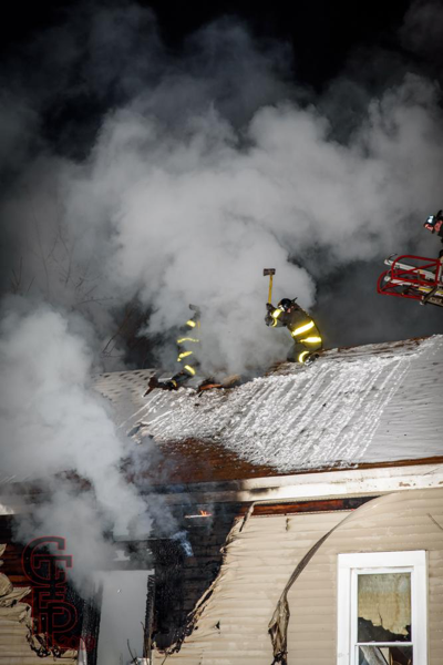 Firefighters vent peak roof with axes in smoke and snow
