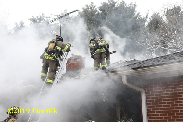 Firefighters on roof of house immersed in smoke