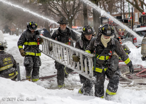 Firefighters carry roof ladder coated with ice at fire scene