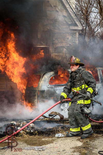 Firefighter prepares to extinguish a minivan engulfed in fire