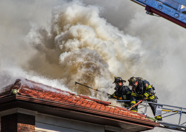 Firefighters vent roof from aerial ladder tip with heavy smoke