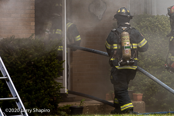 Firefighters enter house on fire with hose
