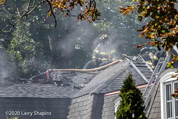 Firefighters on the roof of a house use a cellar nozzle to douse flames in the atti